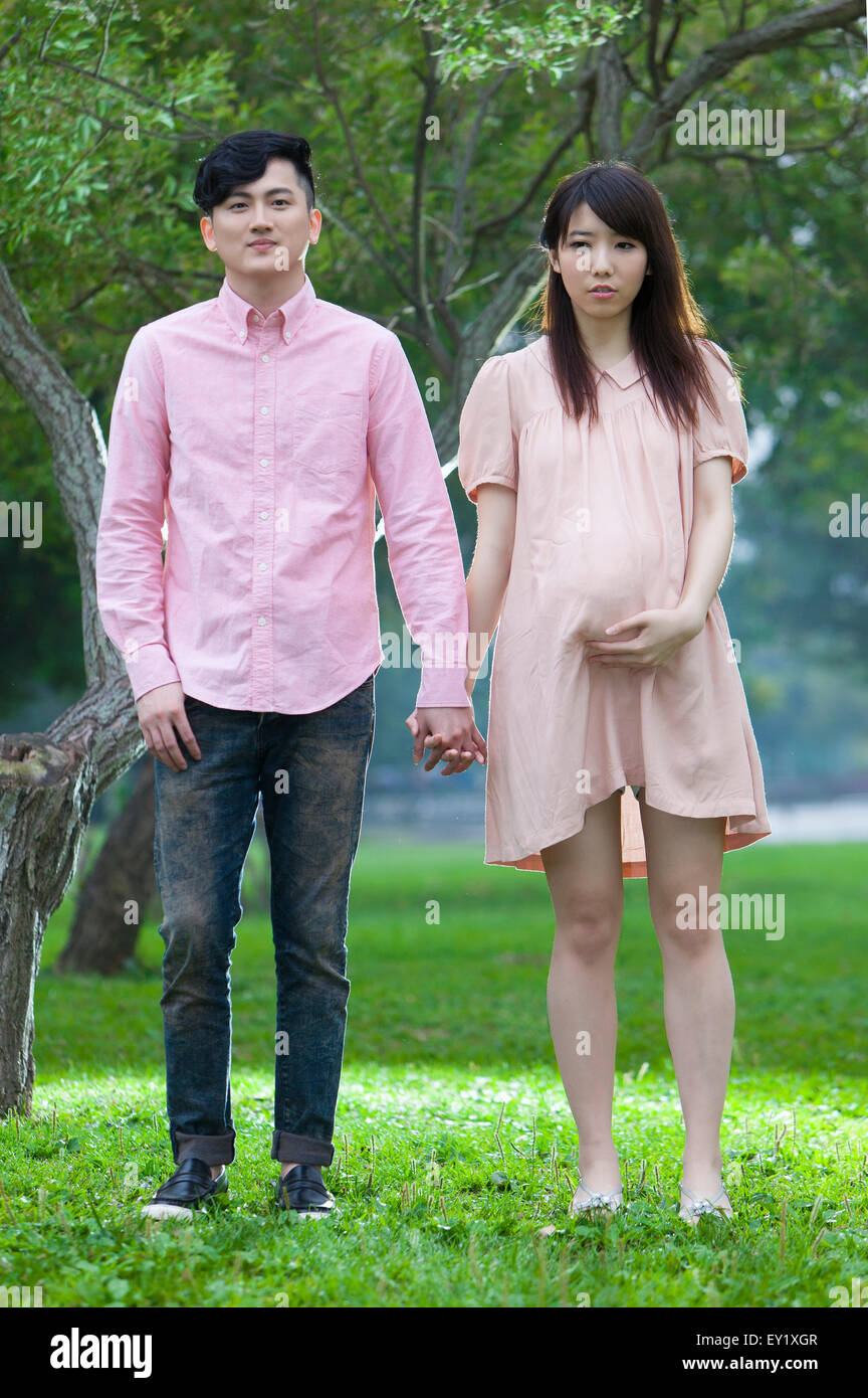Jeune homme et femme enceinte debout sur la pelouse et tenant la main, Banque D'Images