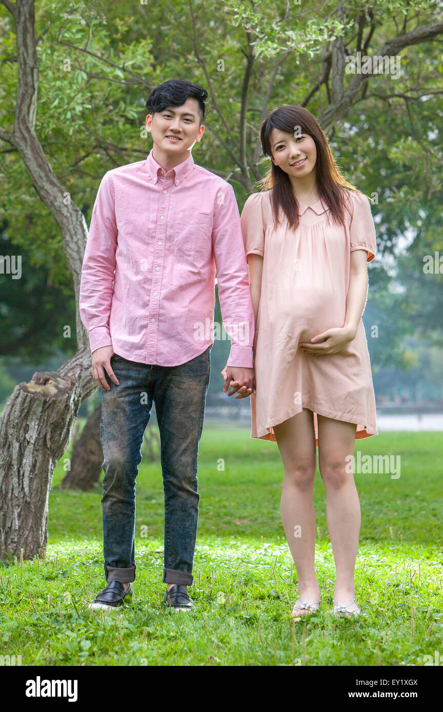 Jeune homme et femme enceinte debout sur la pelouse et tenir la main avec sourire ensemble, Banque D'Images