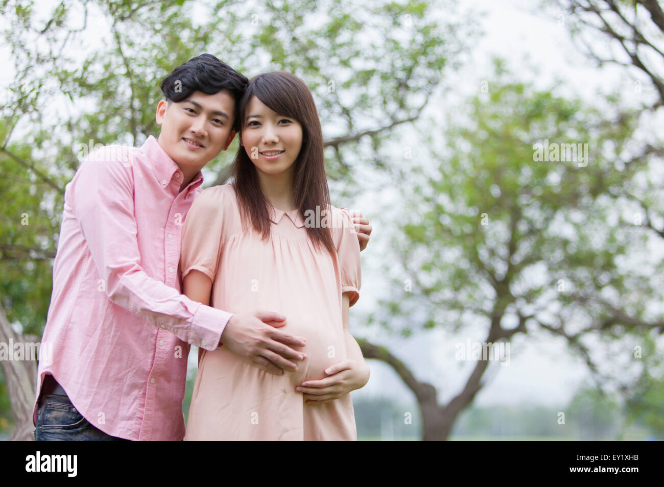 Young man embracing pregnant woman and smiling at the camera, Banque D'Images