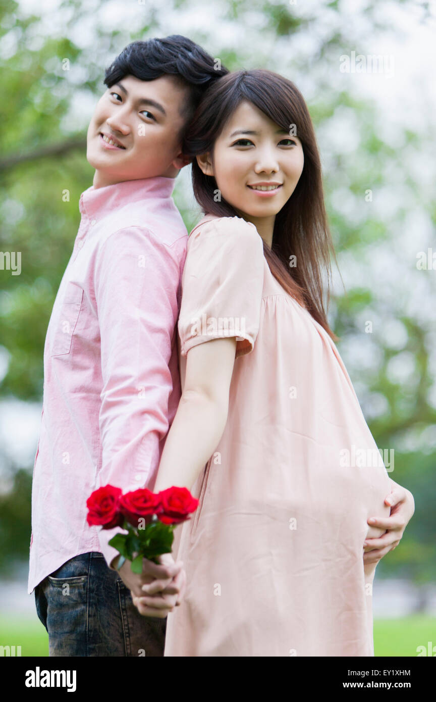 Jeune homme et femme enceinte debout avec dos à dos et tenir la main avec sourire, Banque D'Images