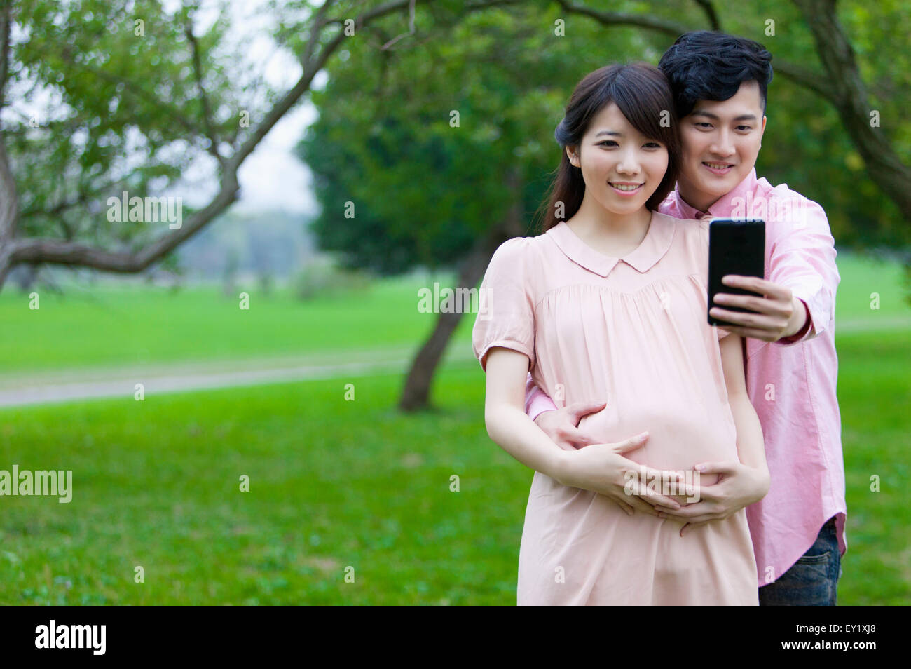 Jeune homme et femme enceinte à au téléphone mobile et prendre des photos avec le sourire, Banque D'Images