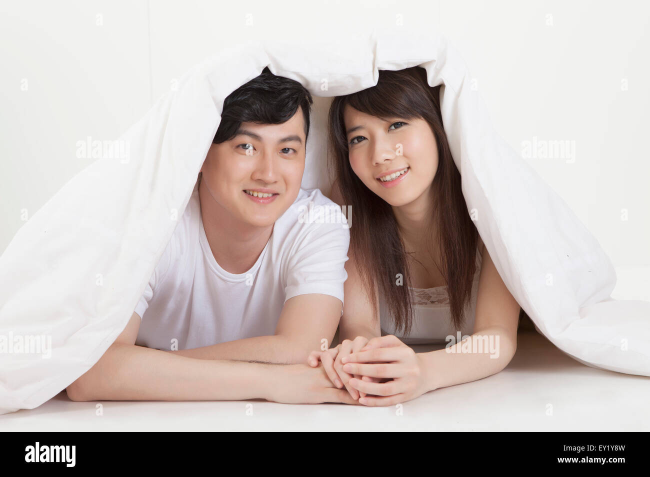 Jeune couple couché à l'avant et souriant à la caméra sous couverture, Banque D'Images