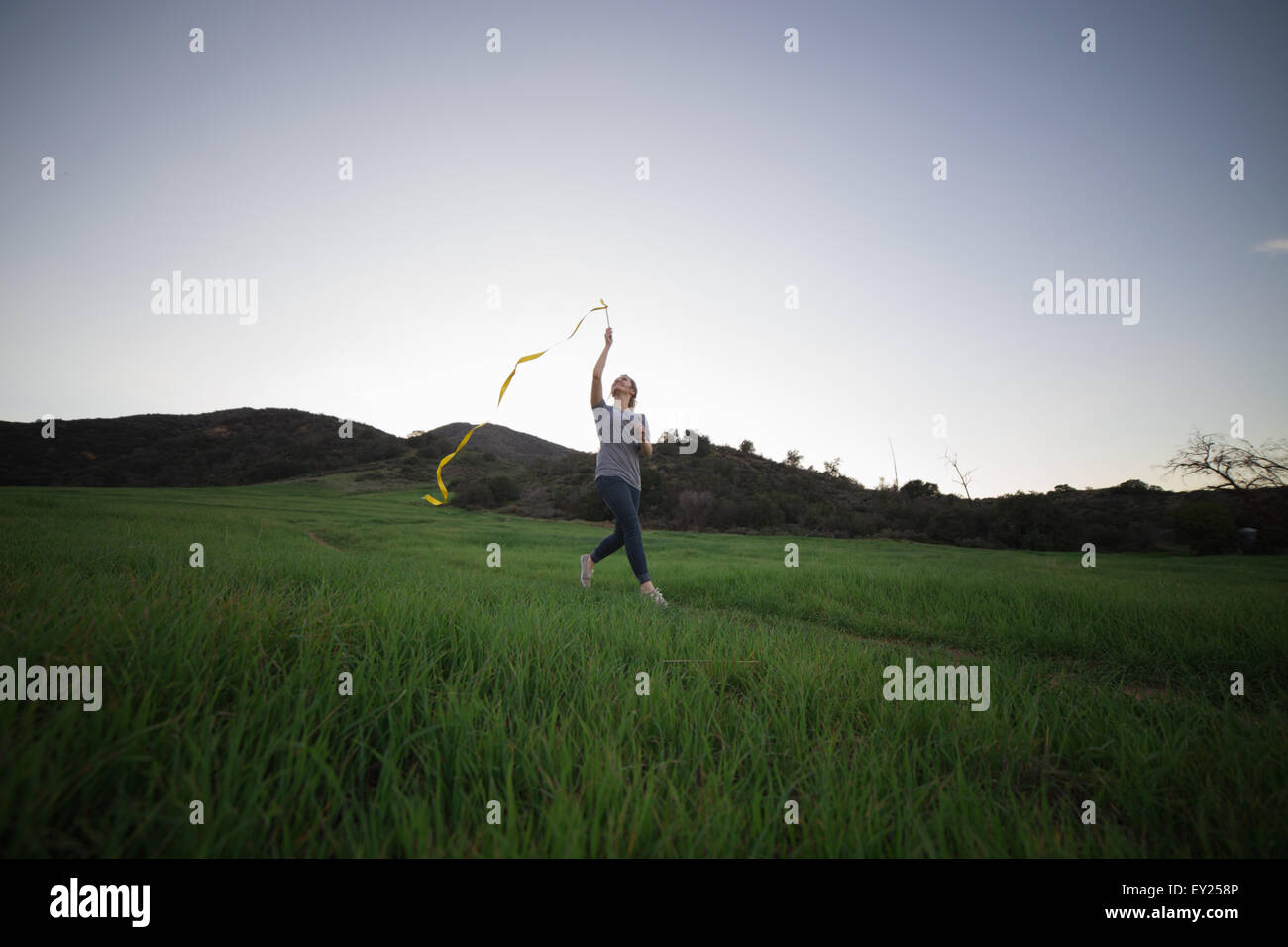 Young woman running in field holding up ruban de danse Banque D'Images