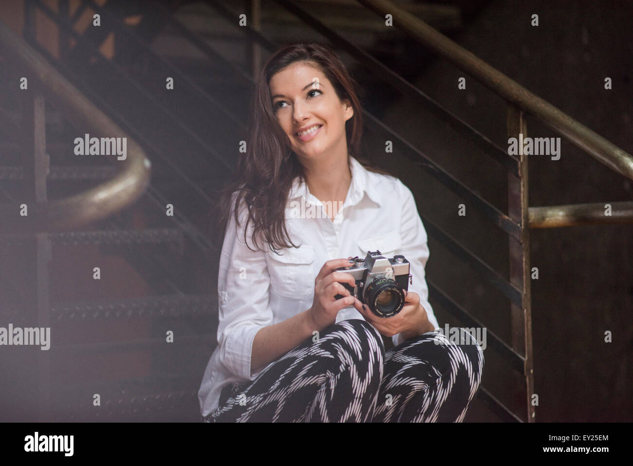 Jeune femme assise sur les marches de l'appareil photo reflex holding Banque D'Images