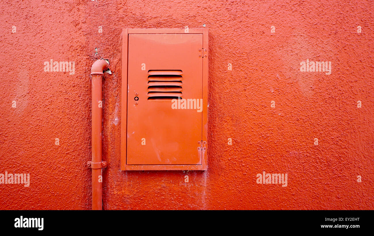 Tuyau métallique et boîtier électrique sur le mur de couleur orange en Burano, Venise, Italie Banque D'Images