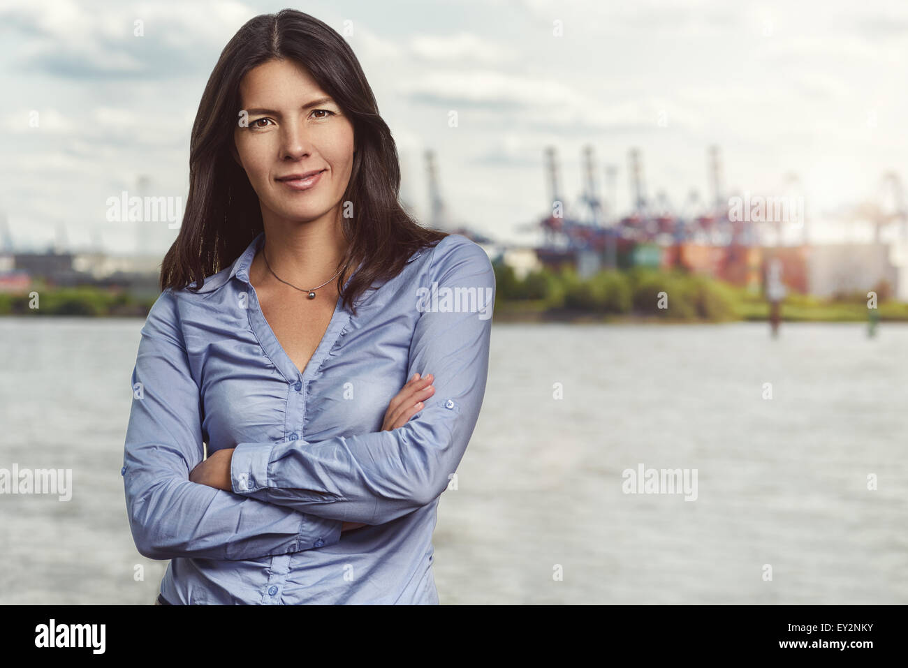 Moitié du corps, tourné d'une certaine jolie jeune femme souriant à la caméra avec passage des bras devant son corps contre ciel voilé River B Banque D'Images