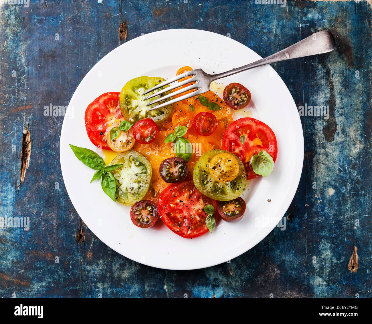 Frais salade de tomates mûres colorés avec de l'huile d'olive et basilic sur fond de bois bleu Banque D'Images