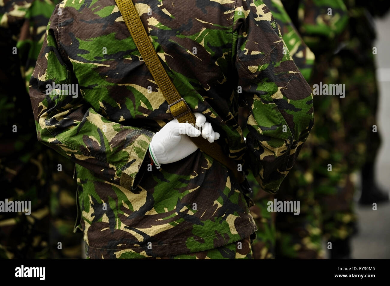 Détail tourné avec un soldat en uniforme de camouflage avec la main derrière le dos, tenant son arme Banque D'Images