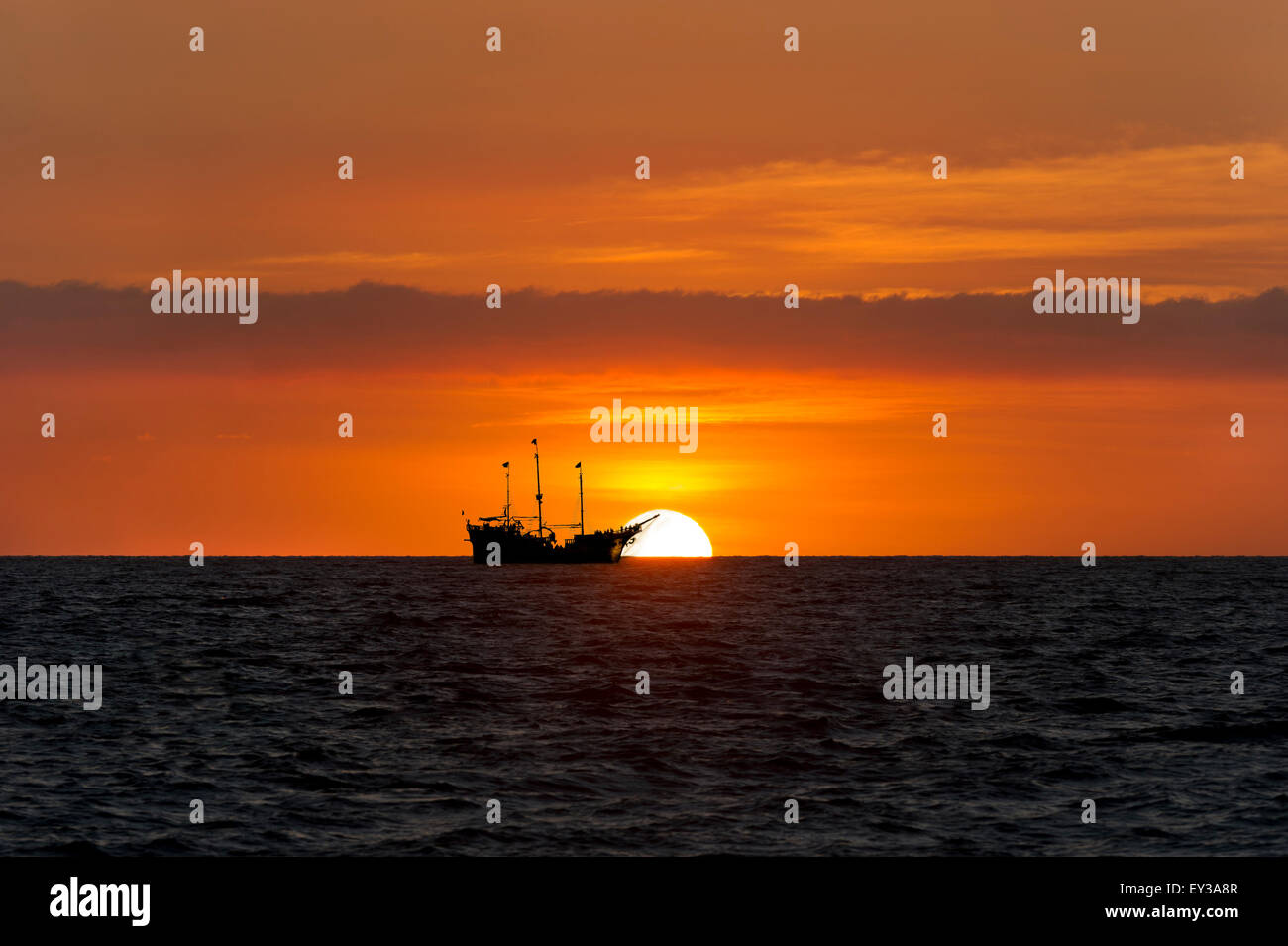 Coucher du soleil est un bateau de pirates en mer voile silhouetté contre un coucher de soleil et un ciel rempli de nuages colorés. Banque D'Images