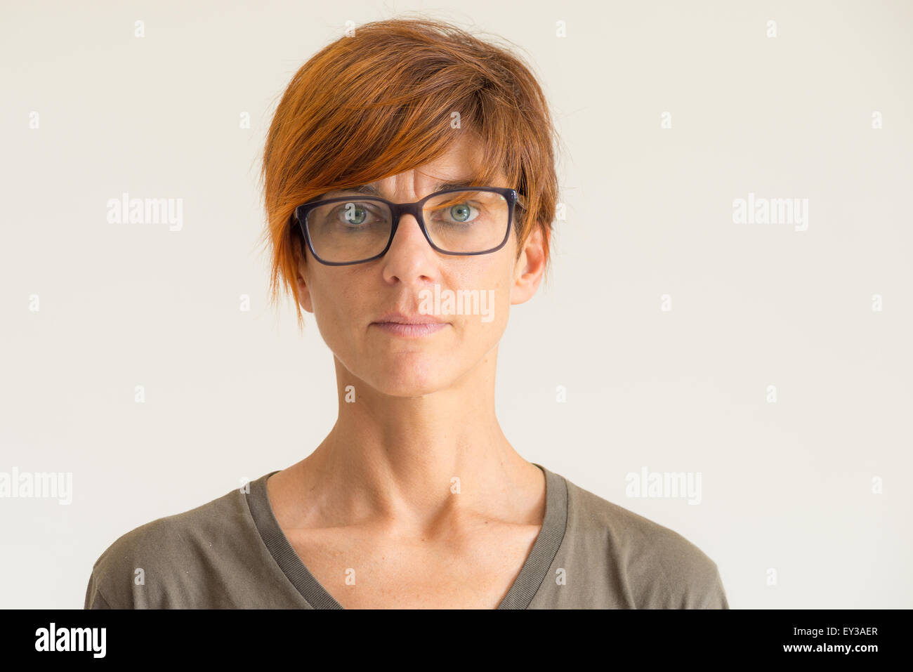 Taille portrait de femme mature avec poils rouges, les yeux verts, les  lunettes et l’expression du visage grave, debout contre le wa Photo Stock