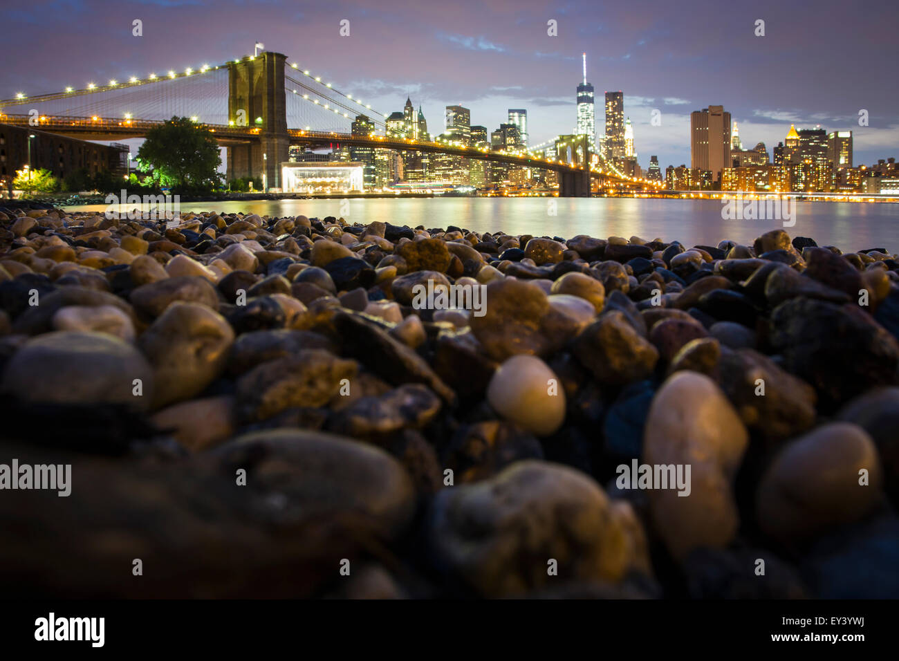 Vue de nuit vers Manhattan de Brooklyn, avec le Pont de Brooklyn enjambant l'East River, la côte rocheuse au premier plan. Banque D'Images
