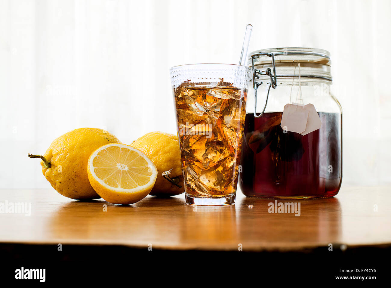 Thé glacé en grand verre, citrons et plateau de table en bois sur Jar Banque D'Images