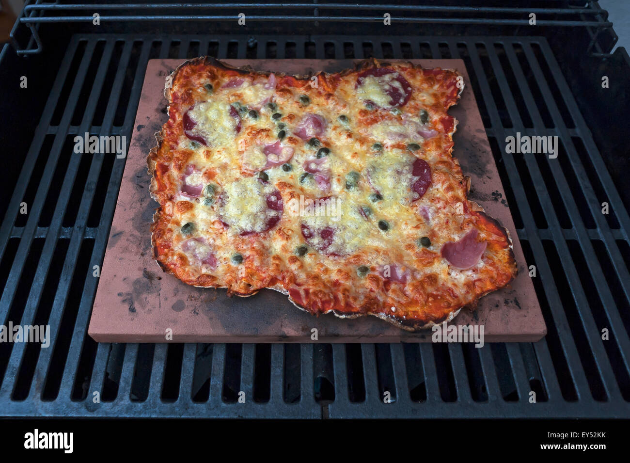 Des pizzas Speziale, tomates, jambon cuit, de salami et de fromage sur une pierre chaude dans un gril à gaz Banque D'Images