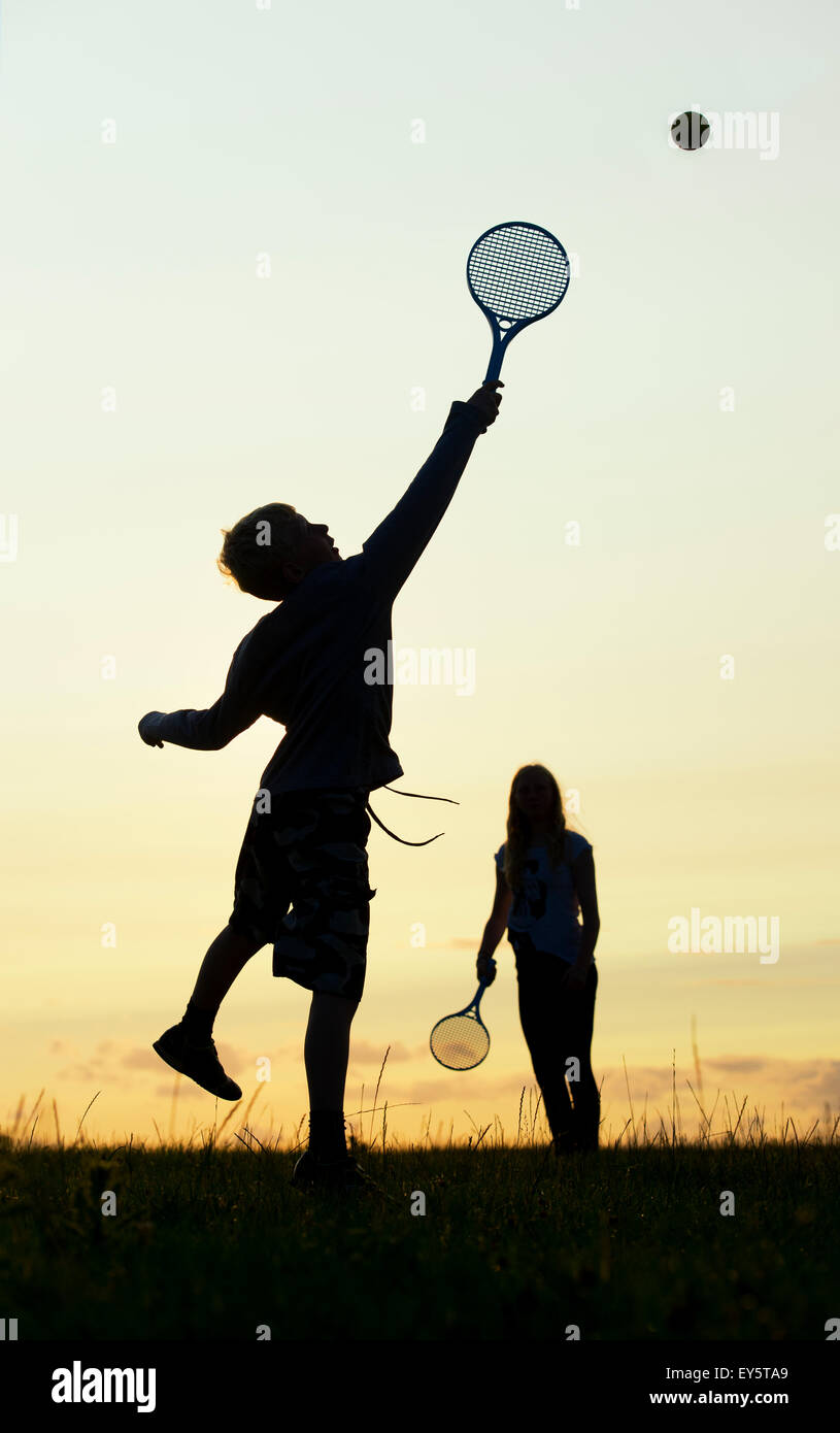 Young Girl and boy playing tennis court au coucher du soleil. Silhouette Banque D'Images