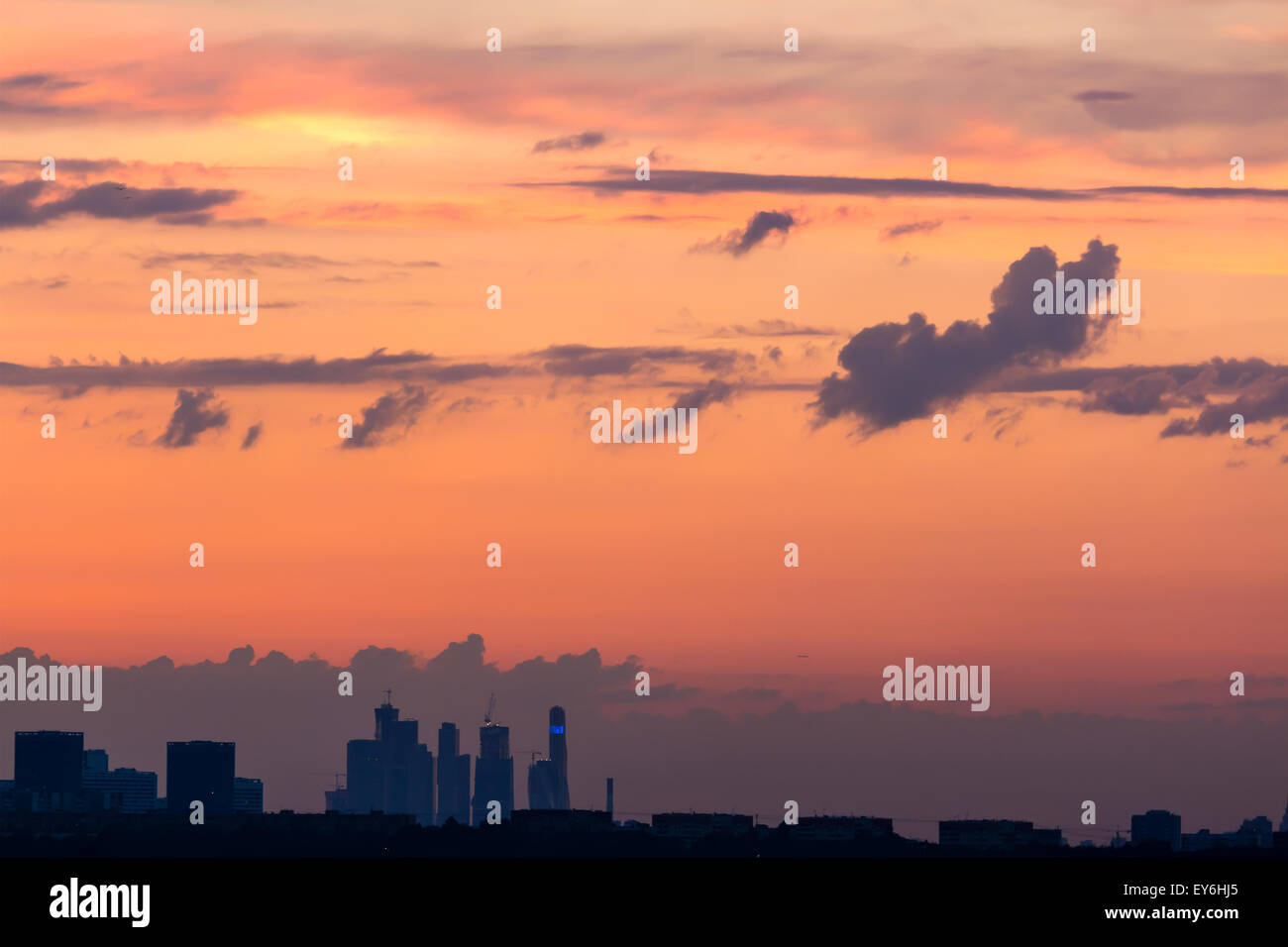 Ciel coloré au coucher du soleil avec des nuages à l'horizon et la silhouette d'édifices de la ville dans une brume légère avec lumières Banque D'Images