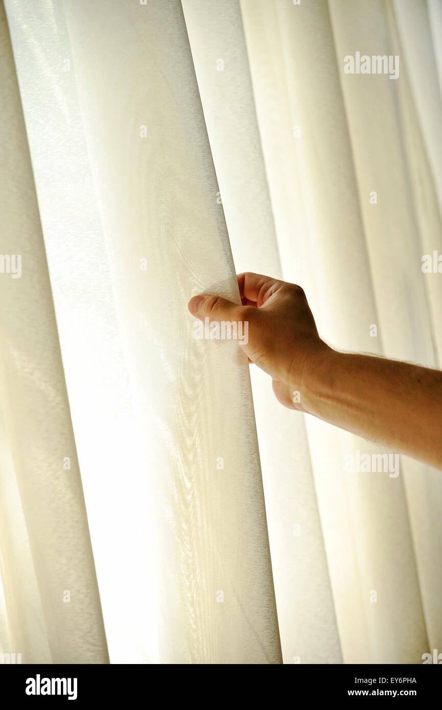 La main d'un homme tirant un rideau de fenêtre pour la lumière du jour chaud d'entrer dans la chambre Banque D'Images