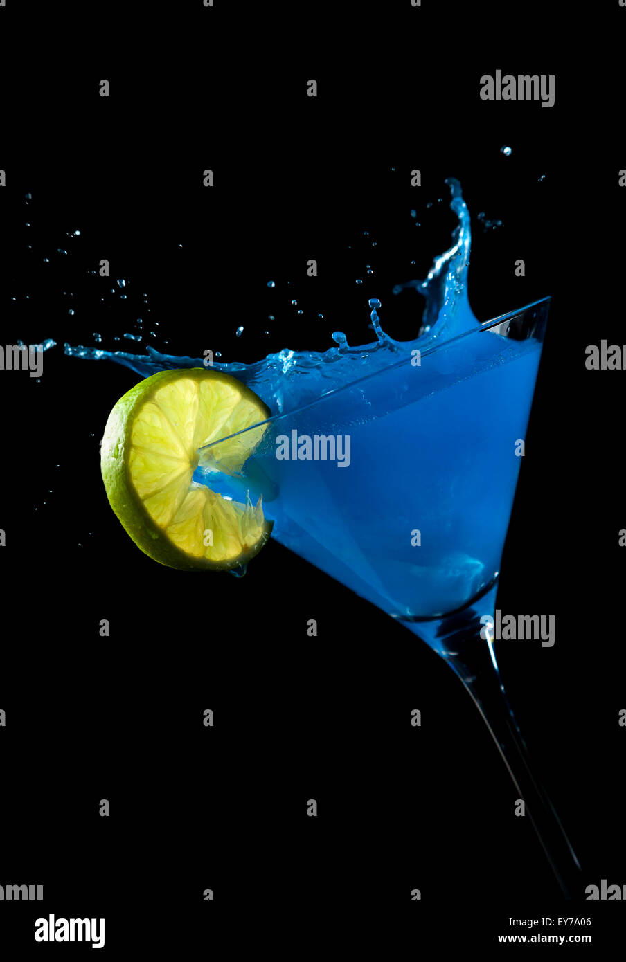 Ice Cube making a splash en verre à cocktail avec cocktail bleu, garni de tranches de lime Banque D'Images