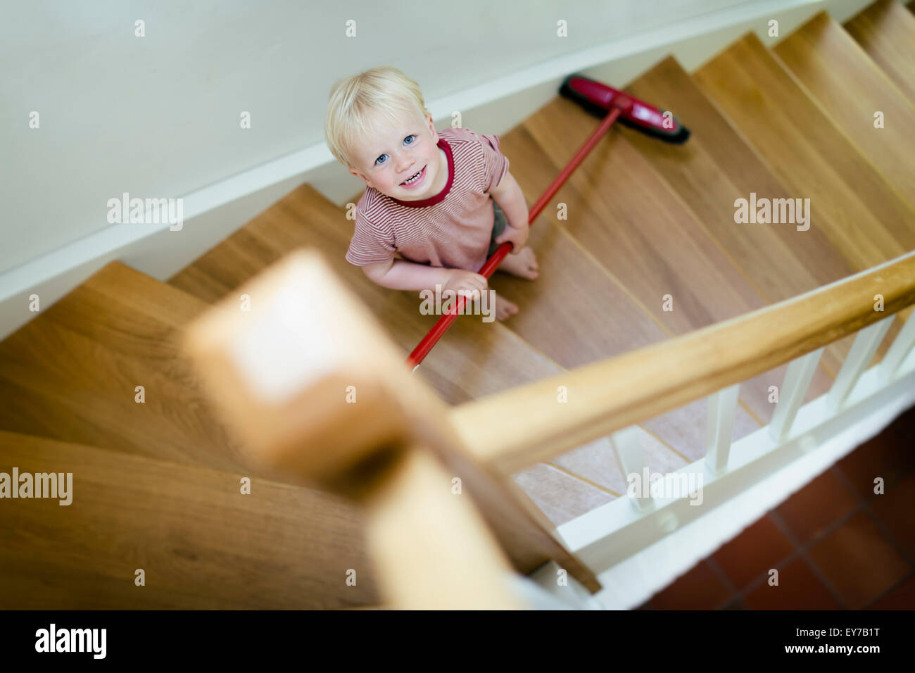 Jeune garçon, 2 ans, balayant un escalier avec un balai. Banque D'Images