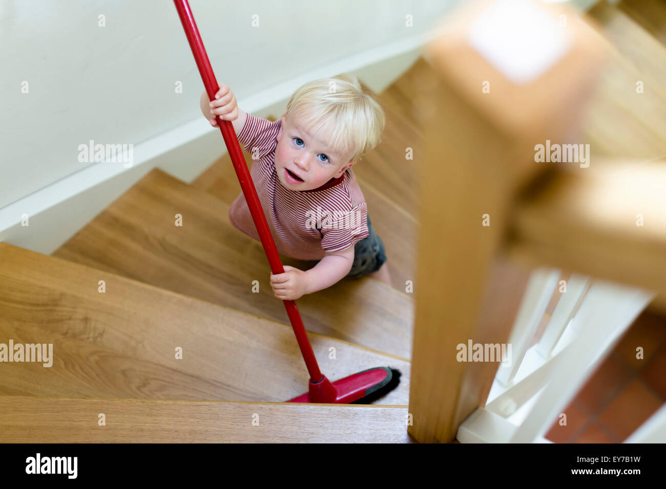 Jeune garçon, 2 ans, balayant un escalier avec un balai. Banque D'Images