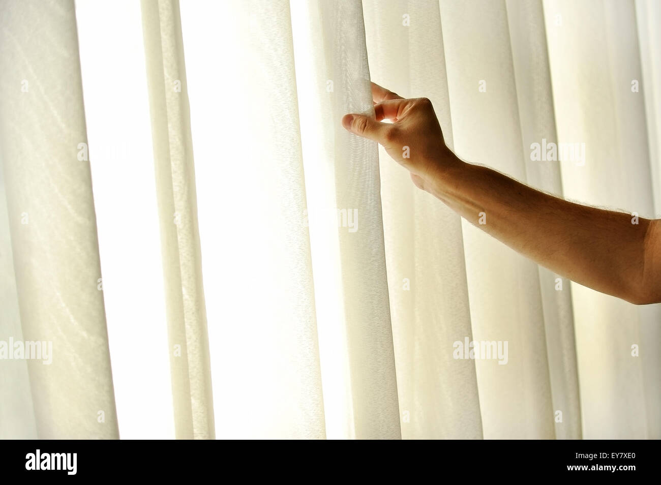 La main d'un homme tirant un rideau de fenêtre pour la lumière du jour chaud d'entrer dans la chambre Banque D'Images