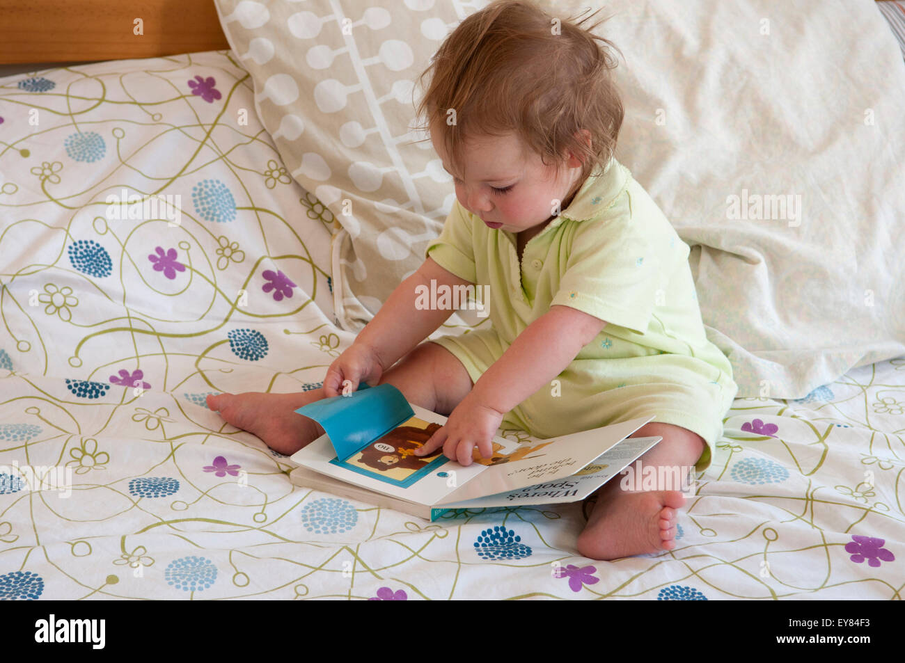 Petite fille assise sur le lit, regardant un livre faisant Banque D'Images