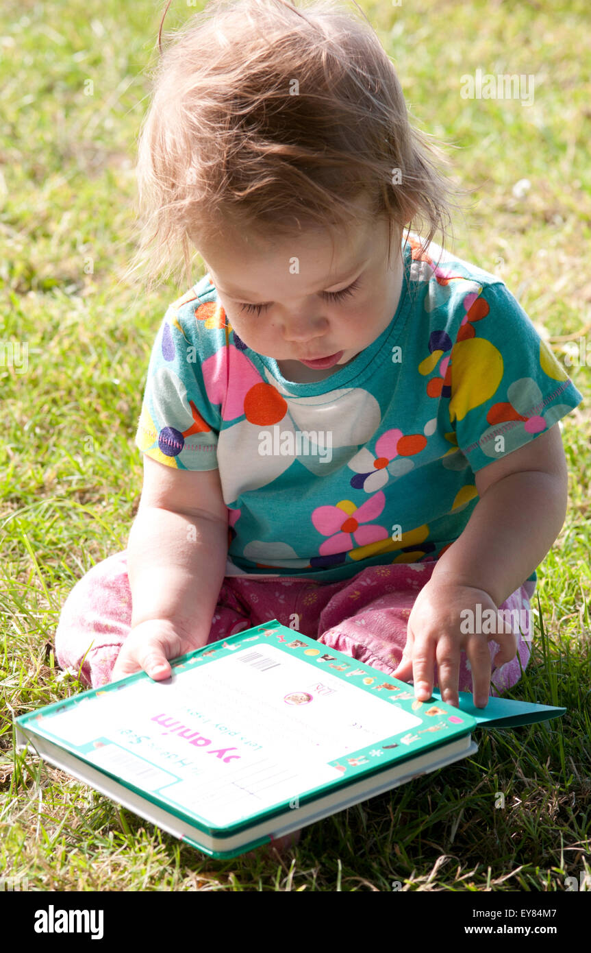 Baby Girl sitting on the grass reading a book Banque D'Images