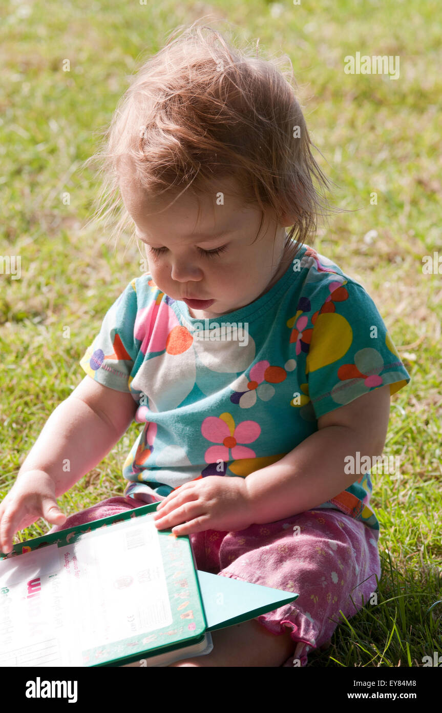 Baby Girl sitting on the grass reading a book Banque D'Images
