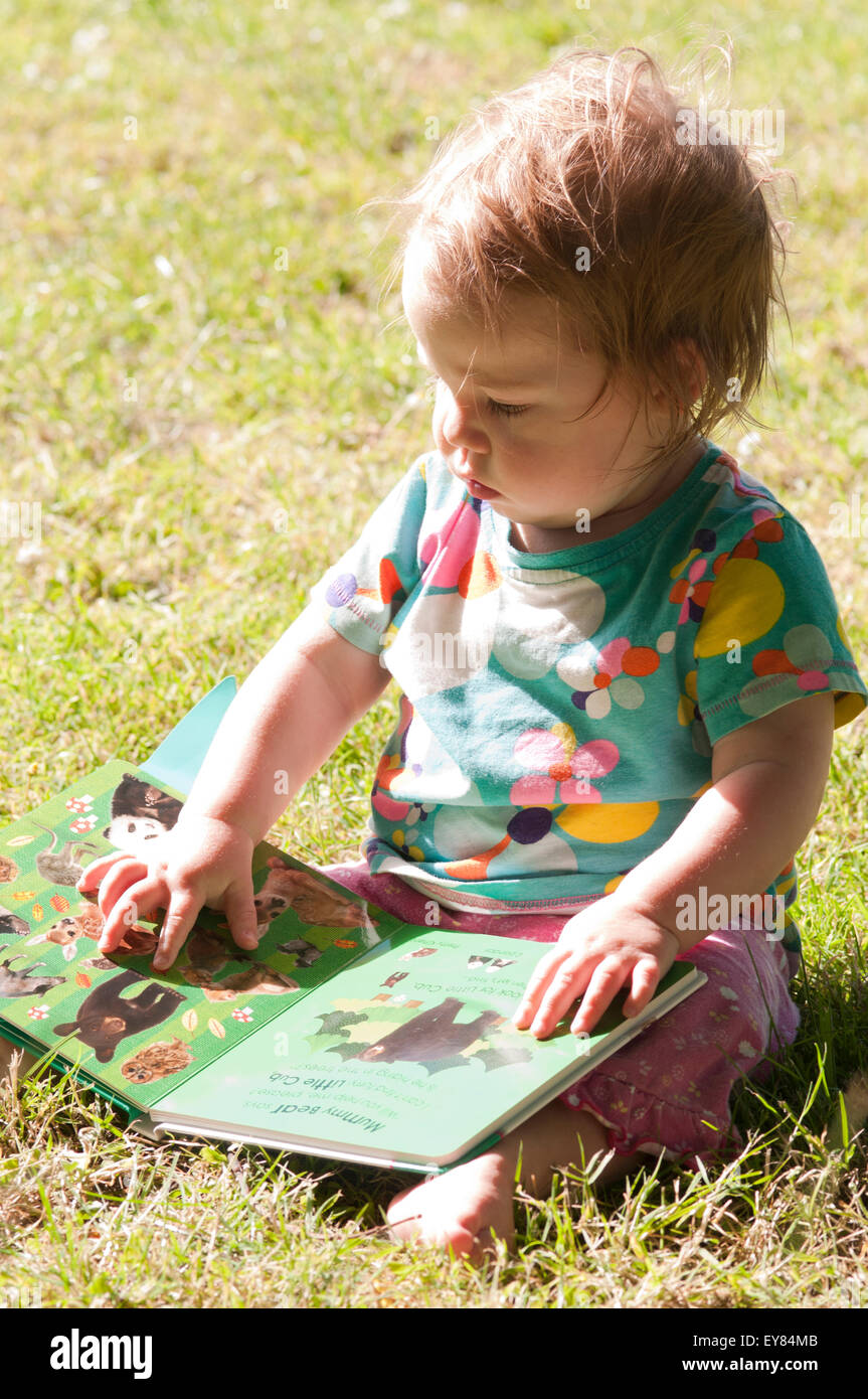 Baby Girl sitting on the grass reading a book Banque D'Images
