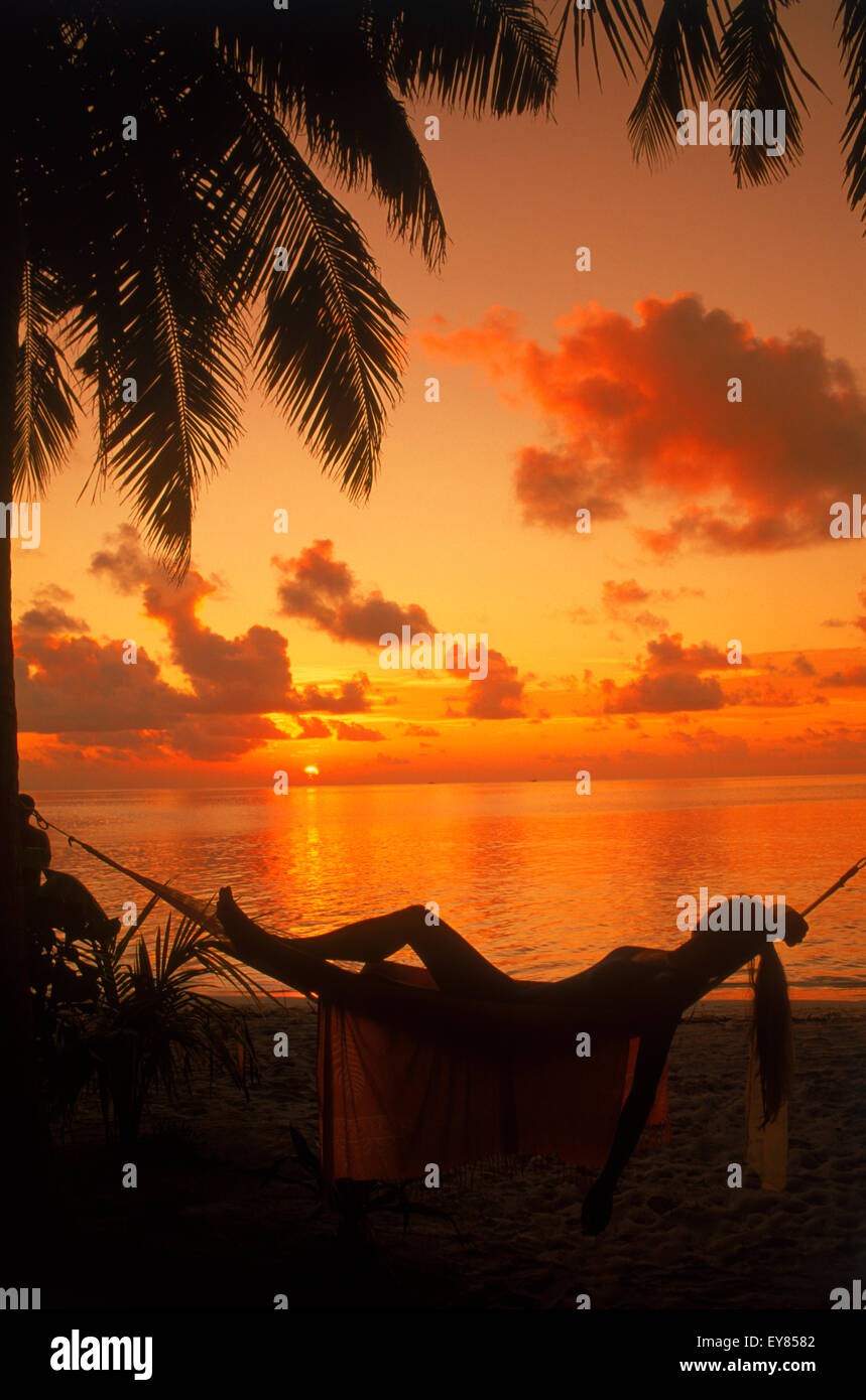 Femme en hamac entre palmiers on tropical island holiday au coucher du soleil Banque D'Images