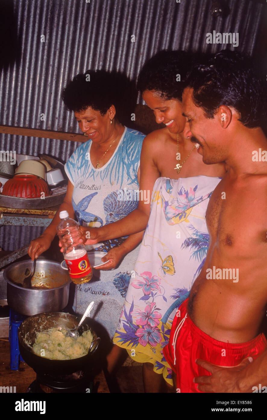 Frère, sœur et mère la cuisson et la préparation des aliments dans la cuisine typique à la maison sur l'île de La Digue aux Seychelles Banque D'Images