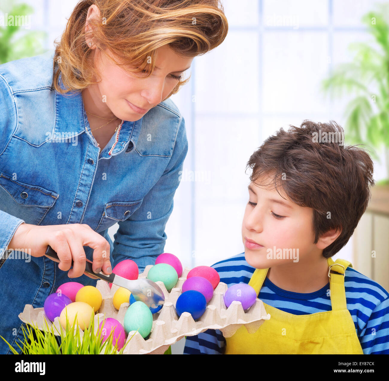 Mère d'enseigner son joli fils à peindre les œufs de Pâques, s'amusant à la maison et avec plaisir les oeufs à colorier Banque D'Images