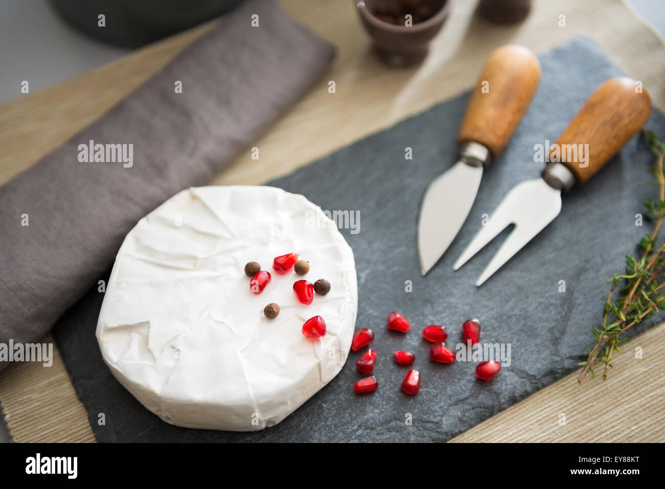 Un nouveau camembert est assis sur une liste de sélection. Graines de grenade, saupoudré sur le dessus, donner une touche de couleur rouge. Sur le plateau de fromage, fromage couteaux sont au repos. Banque D'Images