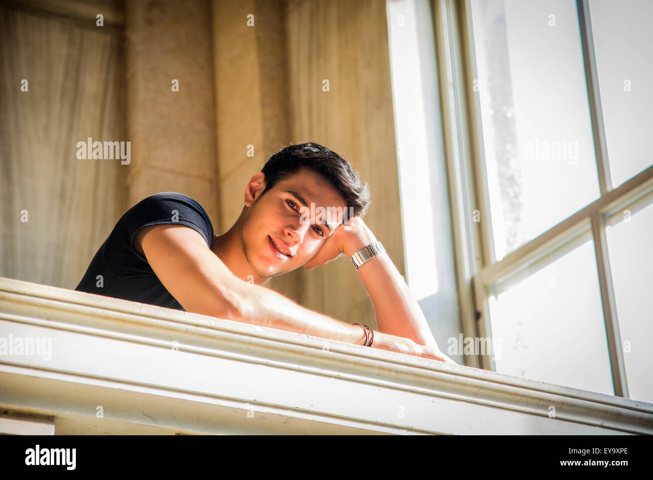 Portrait of Smiling Young Man Leaning on bras croisés contre la rambarde d'escalier en marbre poli à l'intérieur de la construction classique Banque D'Images