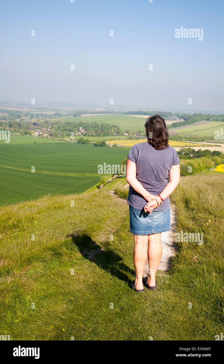 Femme debout sur la pente raide d'escarpe craie Winfield, Wiltshire, England, UK en regardant vers le village de Winfield Banque D'Images