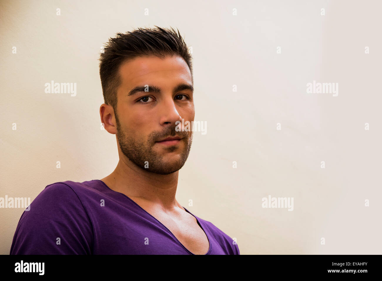 Tête et des épaules de beau jeune homme avec un t-shirt violet, looking at camera, sur fond clair Banque D'Images