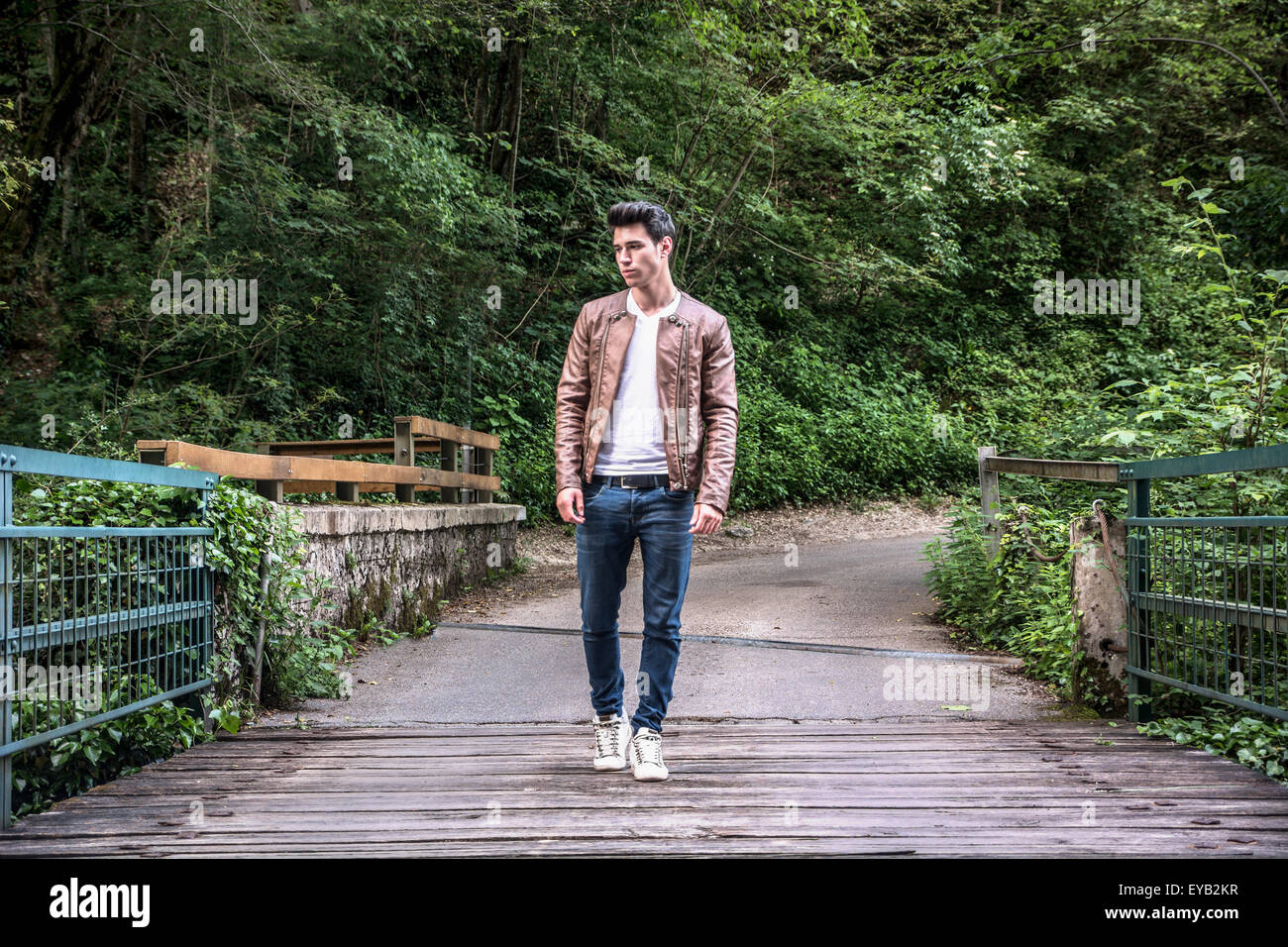 Beau jeune homme de la randonnée dans des paysages de montagne, de traverser un pont dans la forêt à la recherche d'un côté Banque D'Images
