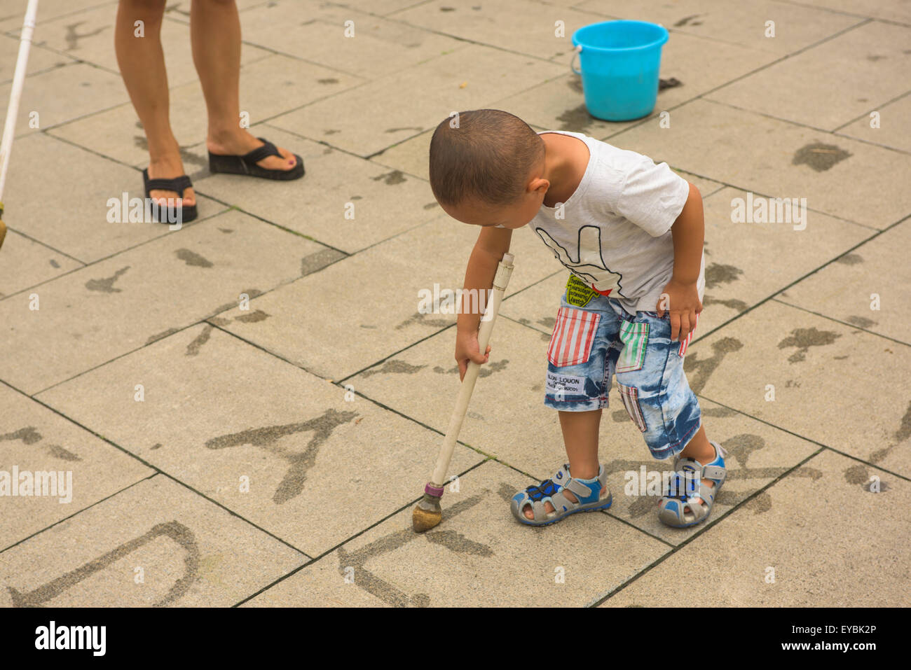 Jeune garçon chinois l'apprentissage de l'écriture à l'aide d'un pinceau et l'eau à Beijing Bei Hai Park, Juillet 2015 Banque D'Images