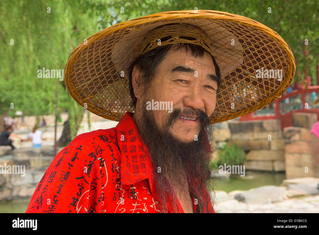 Chinese man wearing coolie-hat, barbe et chemise rouge par le Lac de Kunming à Beijing's Summer Palace - Juillet 2015 Banque D'Images