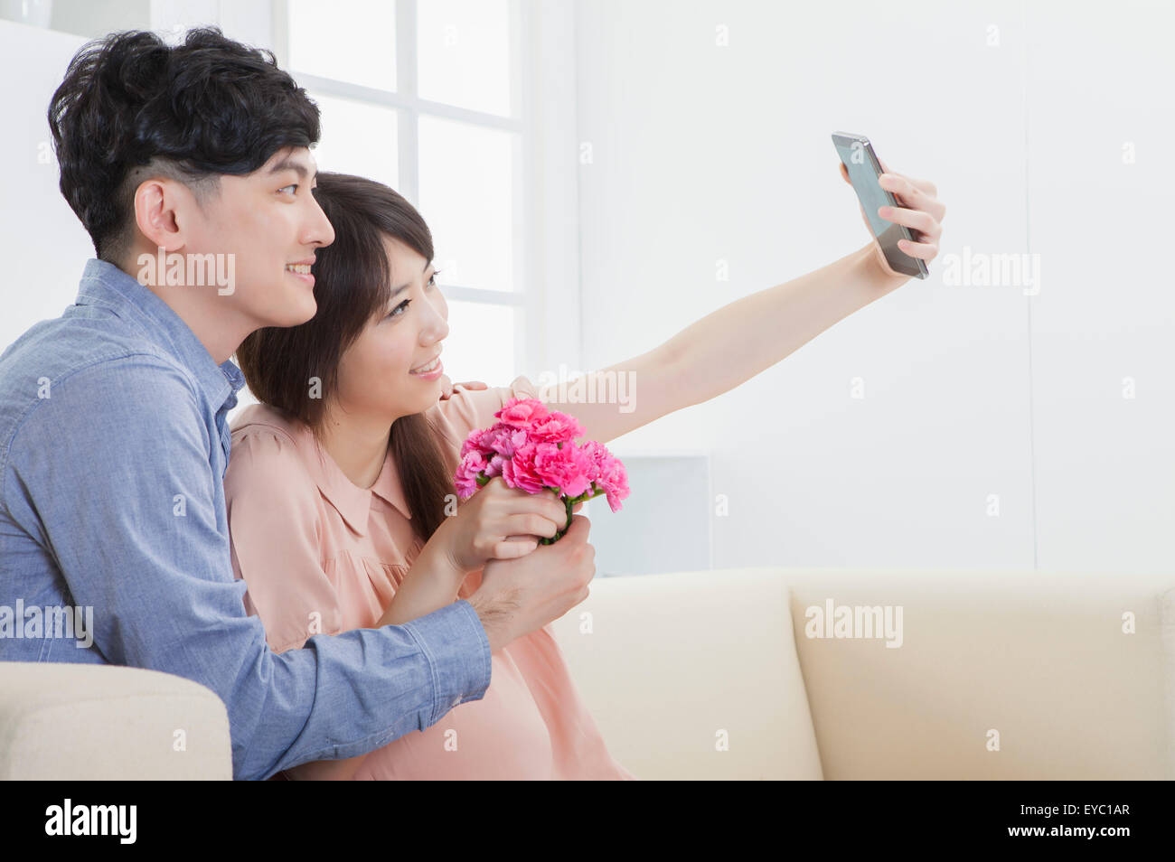 Jeune homme et femme enceinte holding Flowers et prendre des photos avec un téléphone portable, Banque D'Images