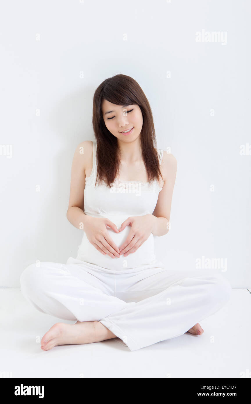 Femme enceinte à la recherche vers le bas et gesticulant avec forme de coeur, Banque D'Images