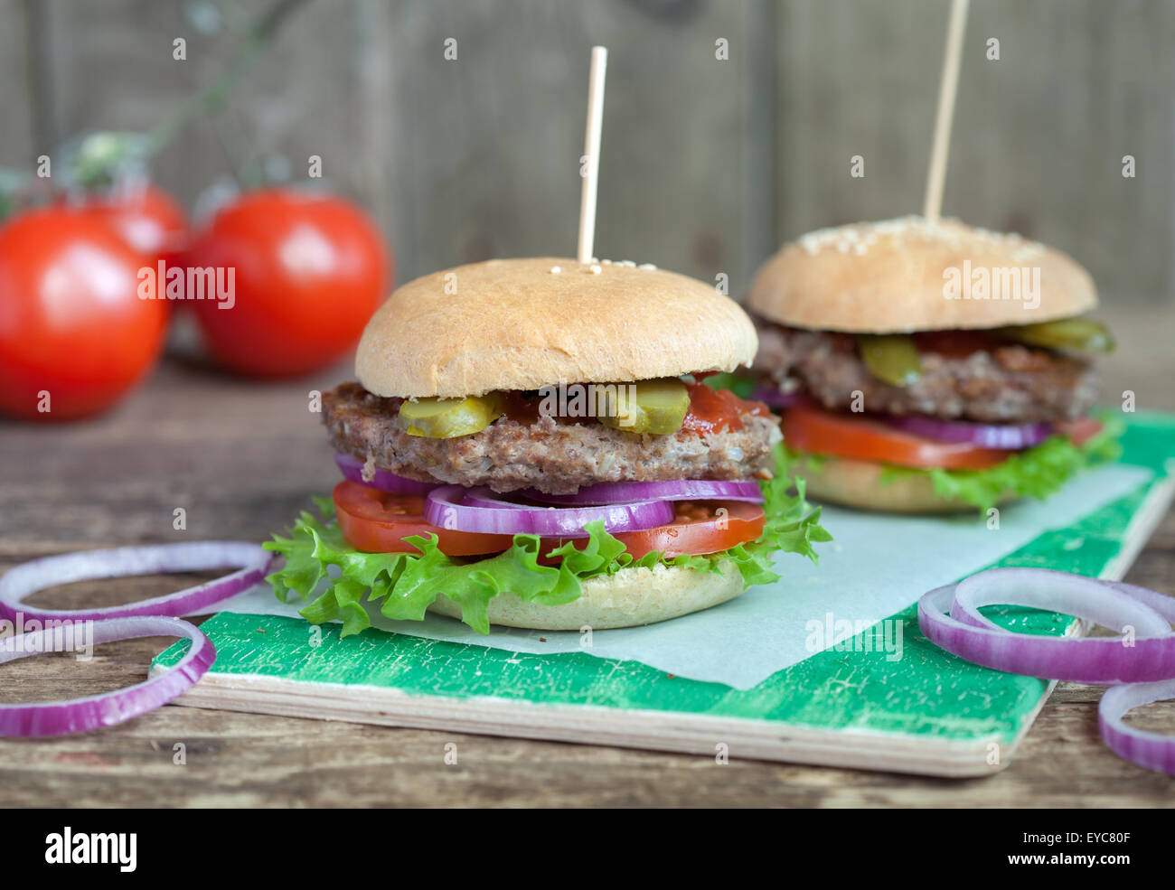 Hamburgers maison avec une salade verte, tomate, oignon rouge, boeuf, concombres et petit pain de blé entier sur une table en bois Banque D'Images