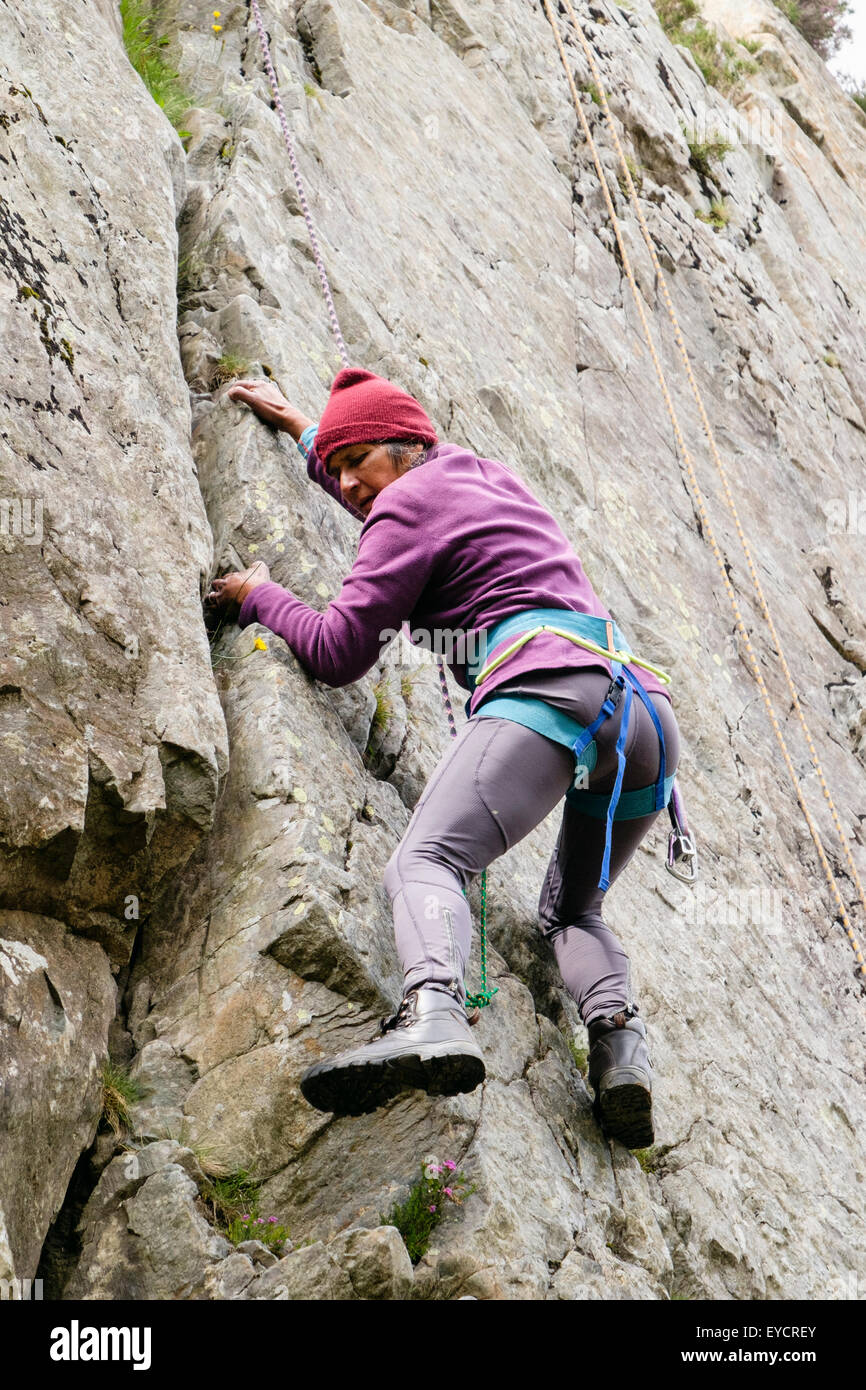 Senior female rock climber avec corde de sécurité haut et le faisceau de grimper d'une fissure dans un rocher. Le Nord du Pays de Galles, Royaume-Uni, Angleterre Banque D'Images