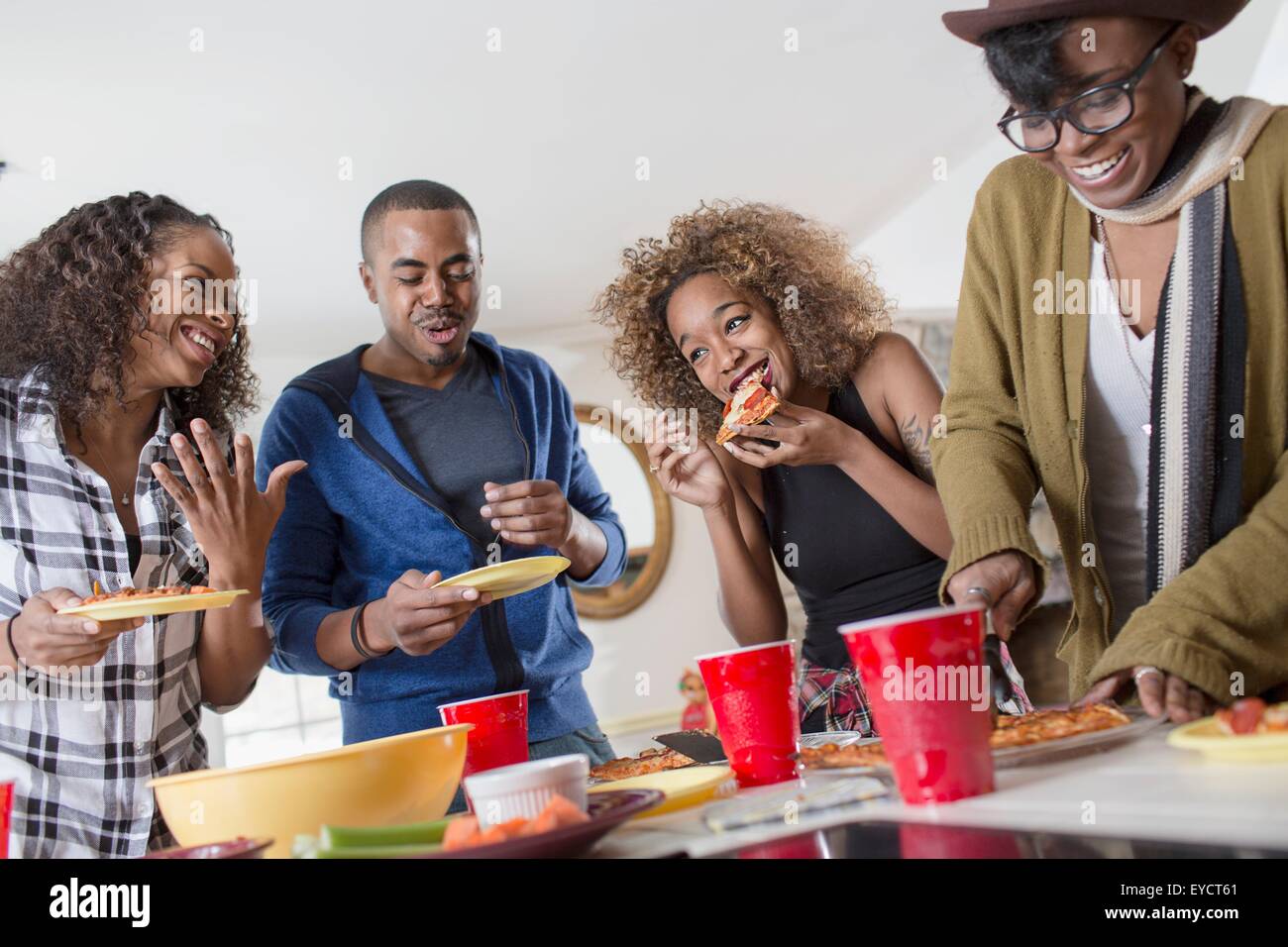 Quatre amis adultes chat et parti manger food in kitchen Banque D'Images