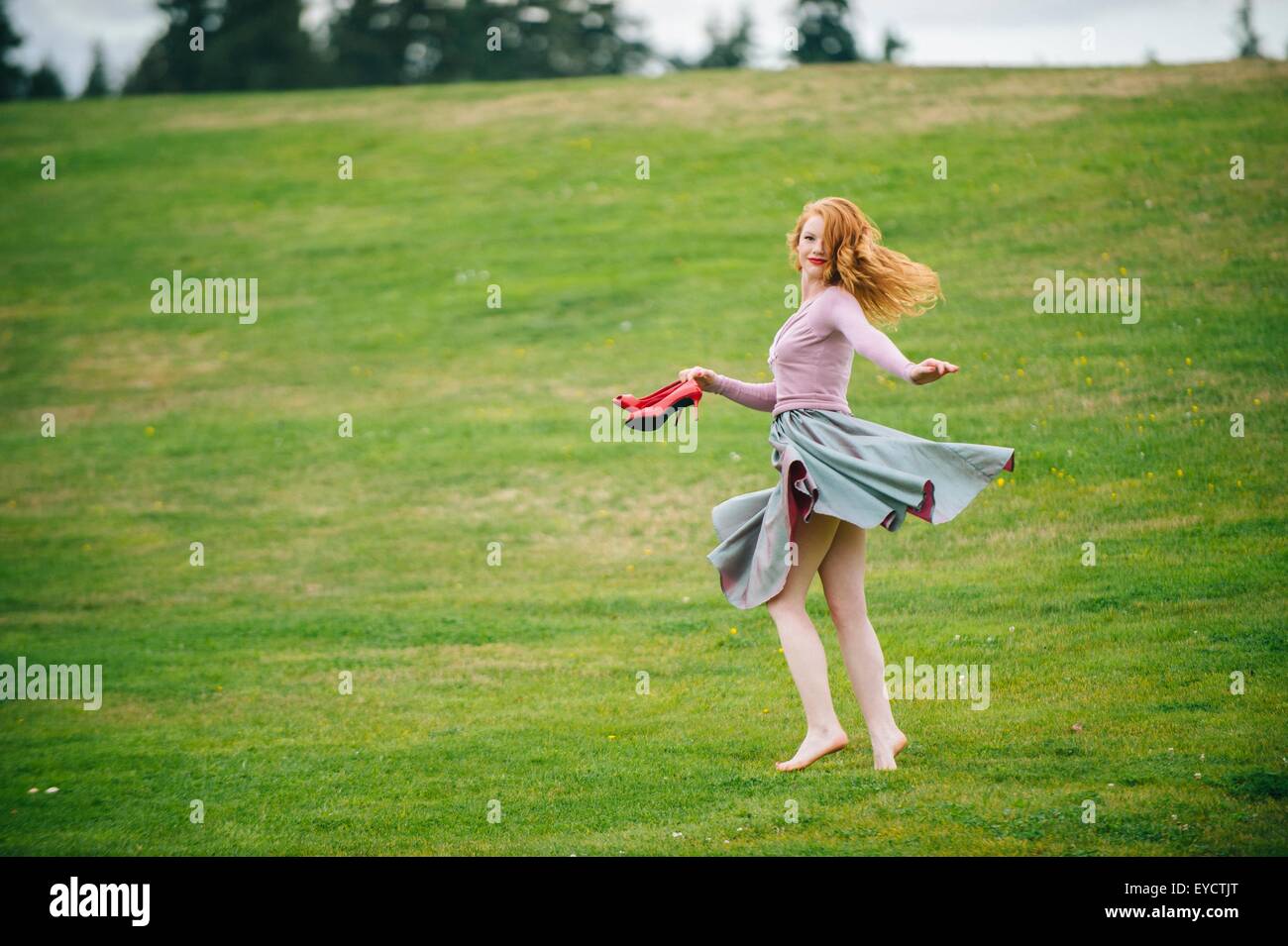 Portrait of young woman dancing in park holding red High heels Banque D'Images