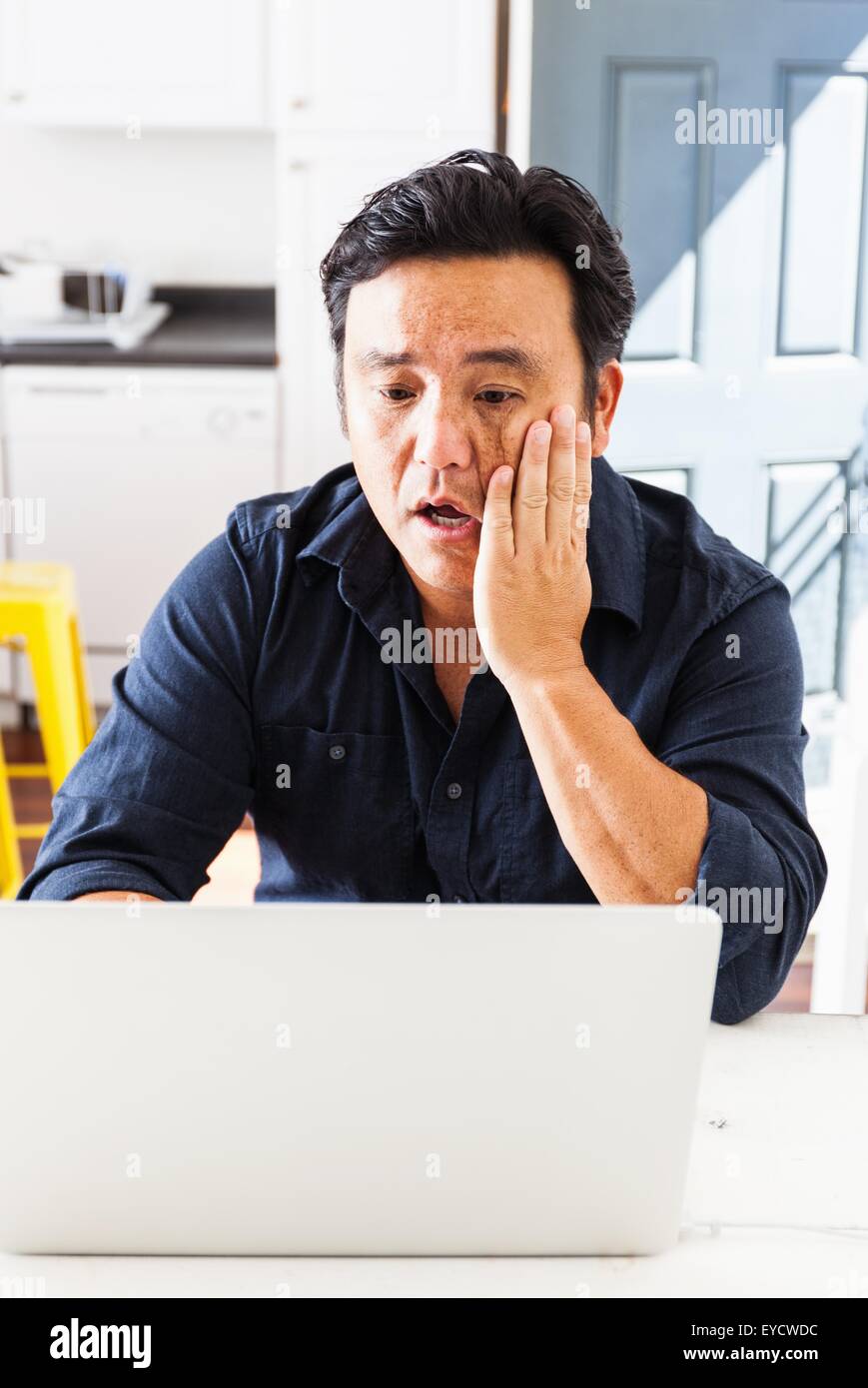 Mature businessman with hand on joue à travailler sur ordinateur portable à la table de cuisine Banque D'Images