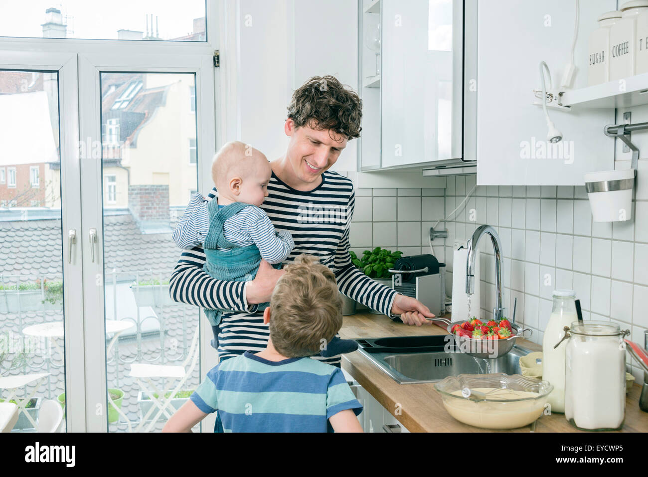 Père prépare la nourriture tout en tenant bébé dans Cuisine Banque D'Images
