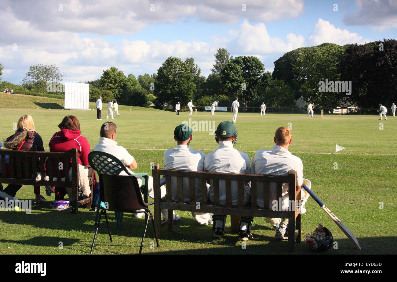 Cricketers watch theri coéquipiers rivaliser dans un match dans un village du Yorkshire près de Rotherham, Angleterre, Royaume-Uni Banque D'Images