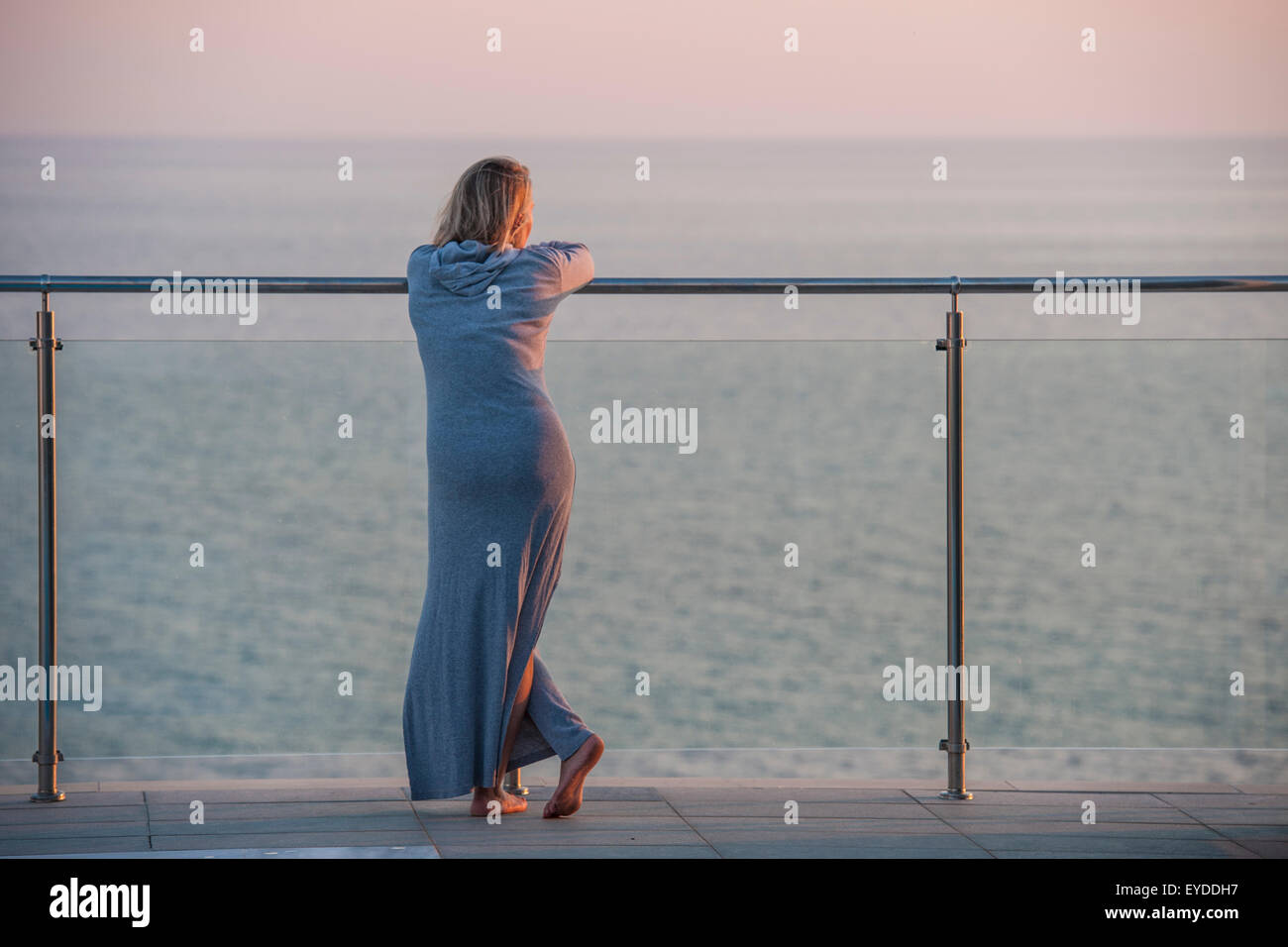Une élégante femme glamour dans une robe de chambre en éponge gris regarde le soleil se coucher sur la côte grecque Banque D'Images