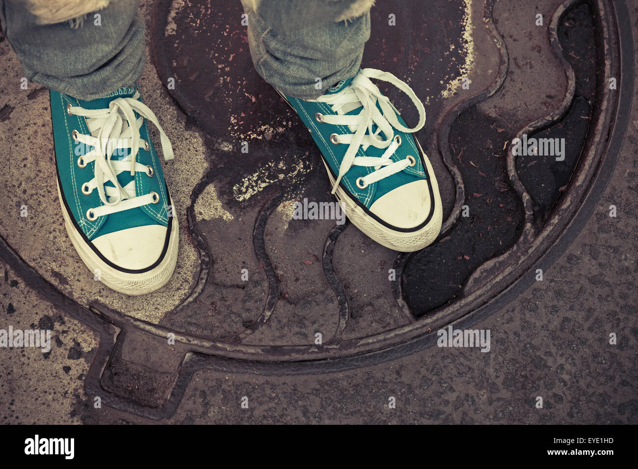 Adolescent en baskets. Pieds de gumshoes rusty se tiennent sur un couvercle de trou d'urbains. Photo Gros Plan avec focus sélectif et vintage Banque D'Images