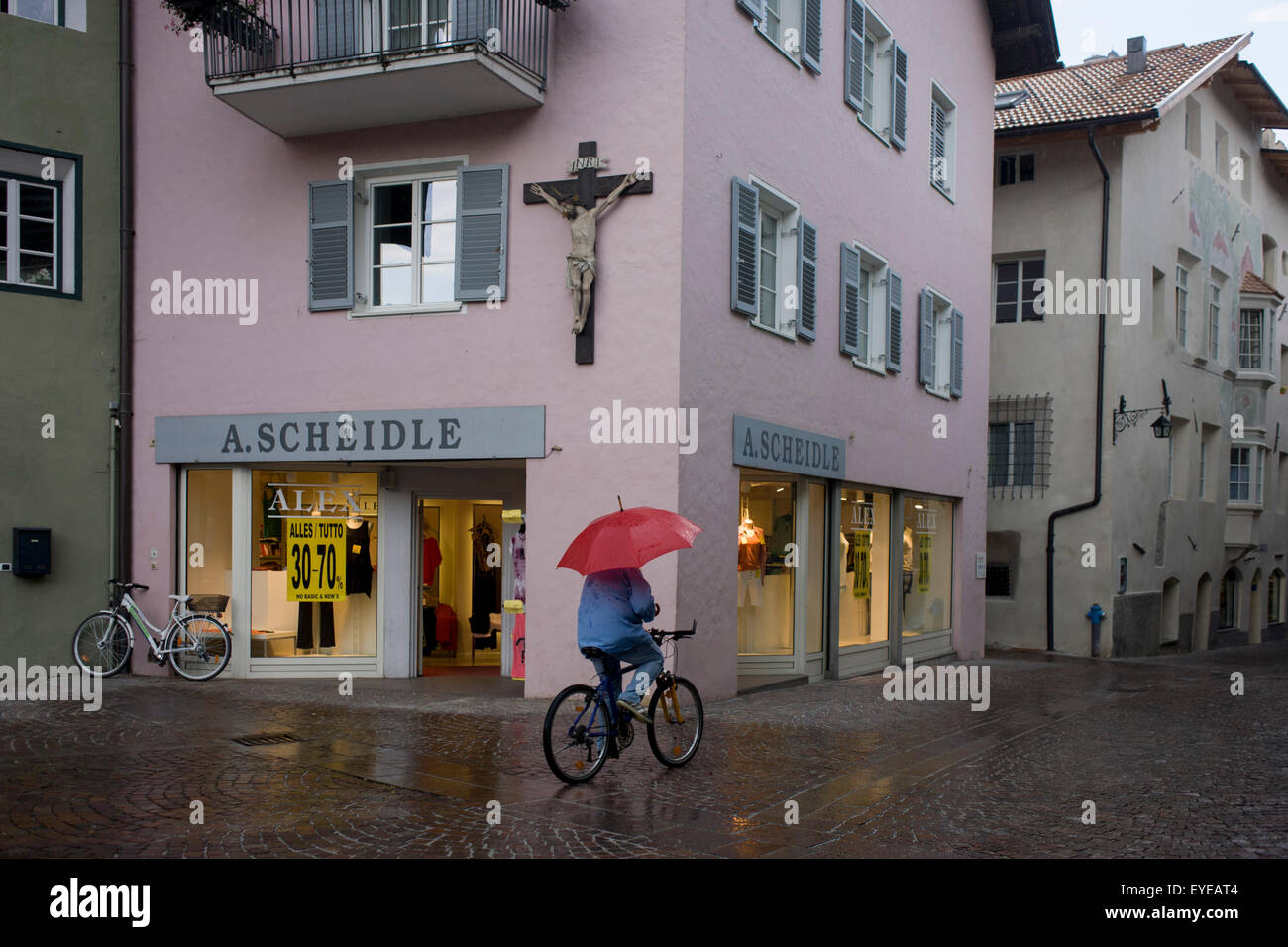 L'exercice cycliste parapluie rouge promenades towartds boutique, sous de grands crucifix dans Klausen-Chiusa ville italienne dans le Tyrol du sud. Banque D'Images